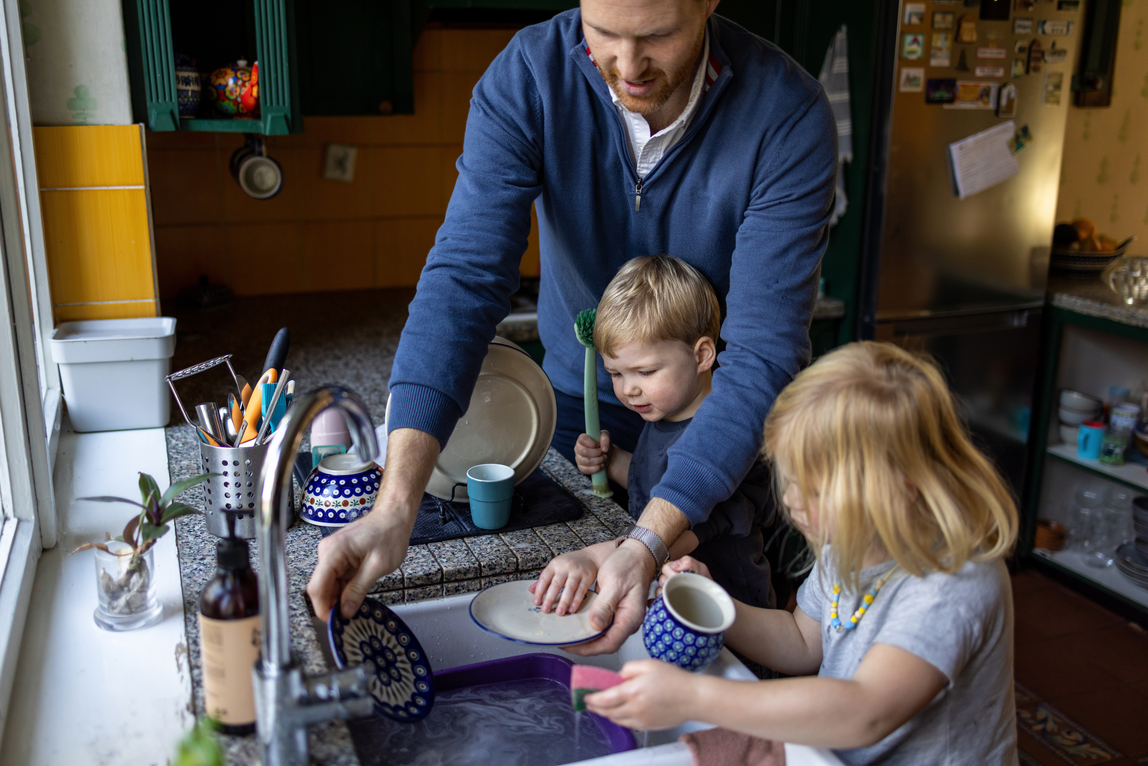 A stay-at-home father washes dishes with his two kids