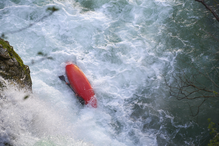 Kayak on a wild river turned upside down, the man inside trying to turn it back up