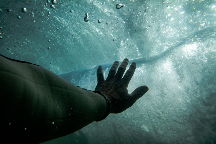 A hand underwater reaching toward a wave