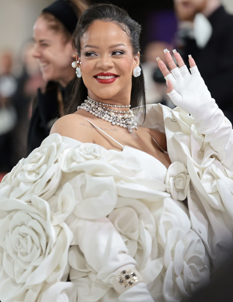 Rihanna waving at an event wearing a large dress with rosettes
