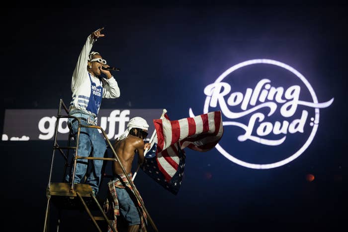 A$AP Rocky standing on top a piece of scaffolding performing as someone next to him waves a flag during Rolling Loud