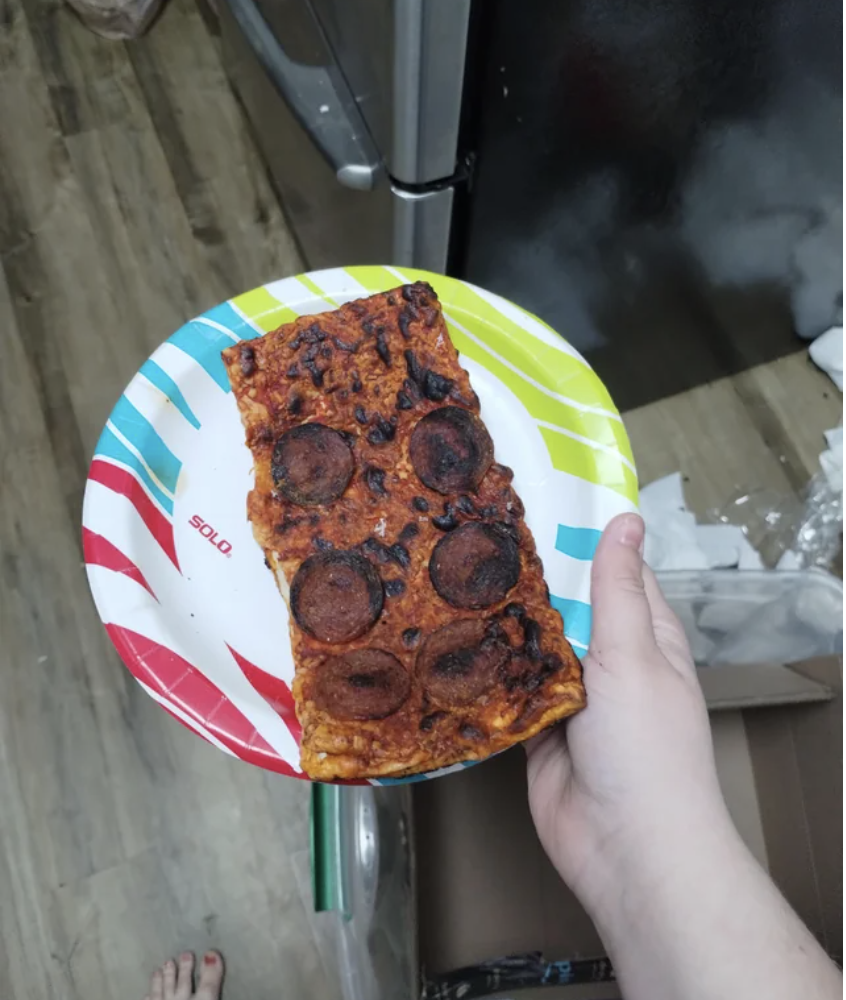 Someone holding a slice of burnt thin Sicilian pizza with burnt pepperoni