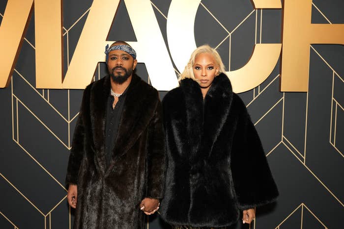 The couple wearing matching fur-like coats and holding hands as they pose for the camera at a media event