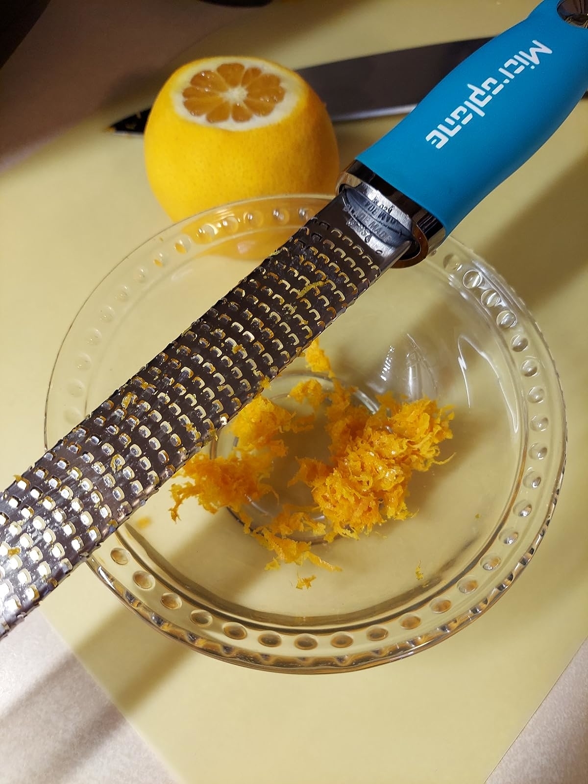 microplane with a blue handle over a bowl of orange zest
