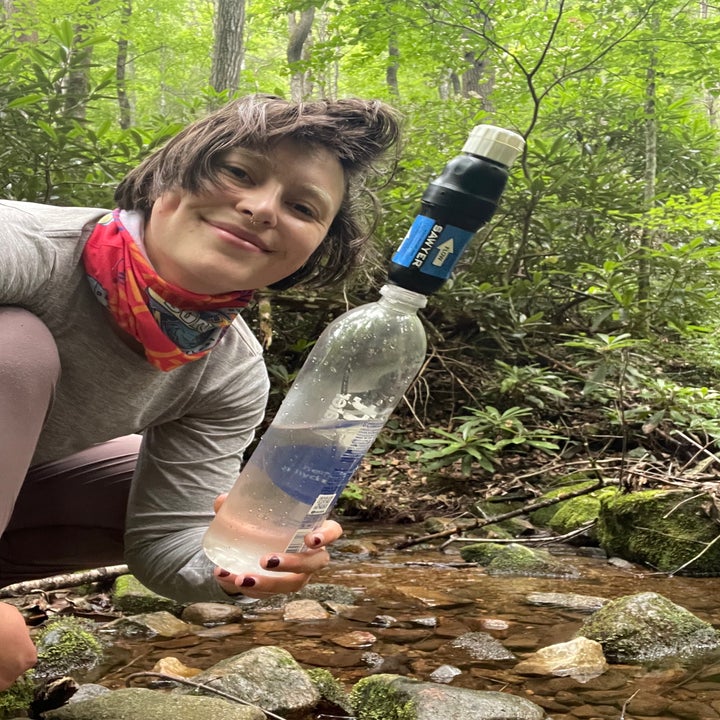 the writer holding the screw-top filter on a smart water bottle by a stream