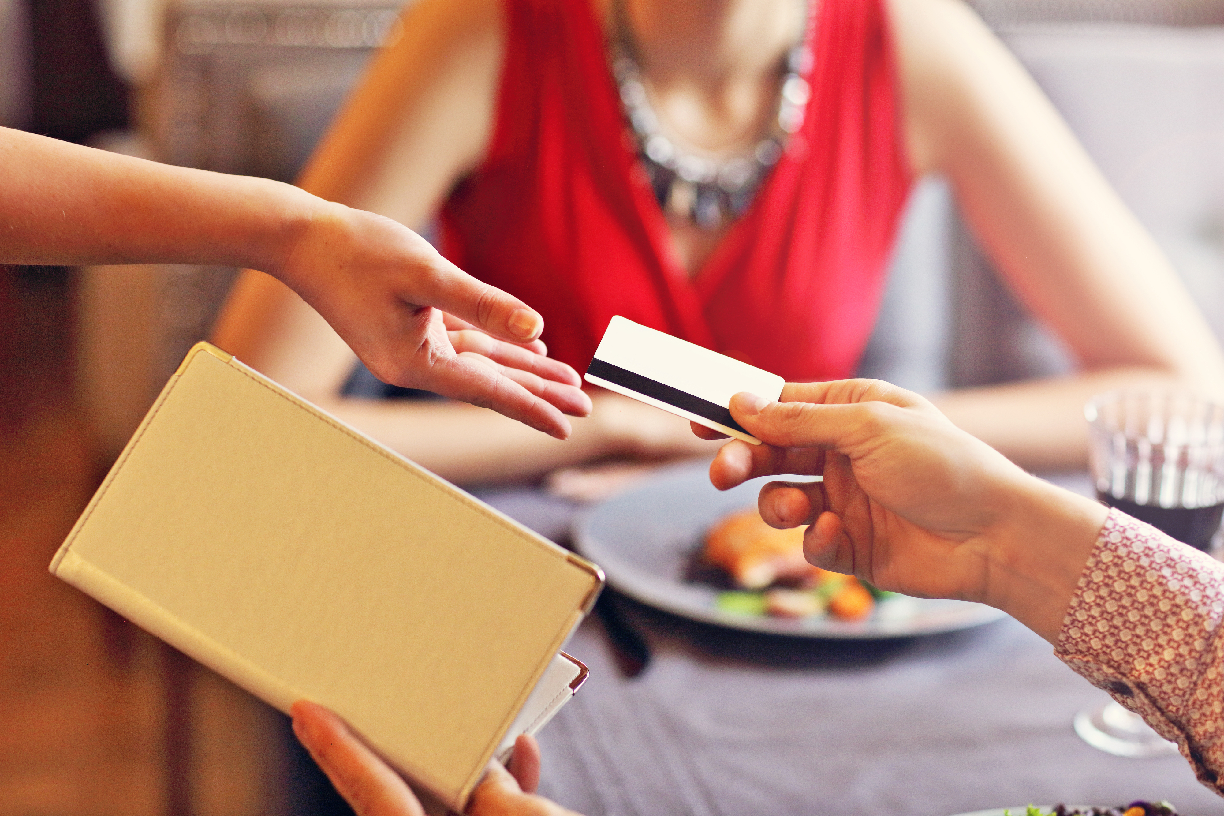 A person hands a credit card to a waiter to pay for their and their date&#x27;s dinner