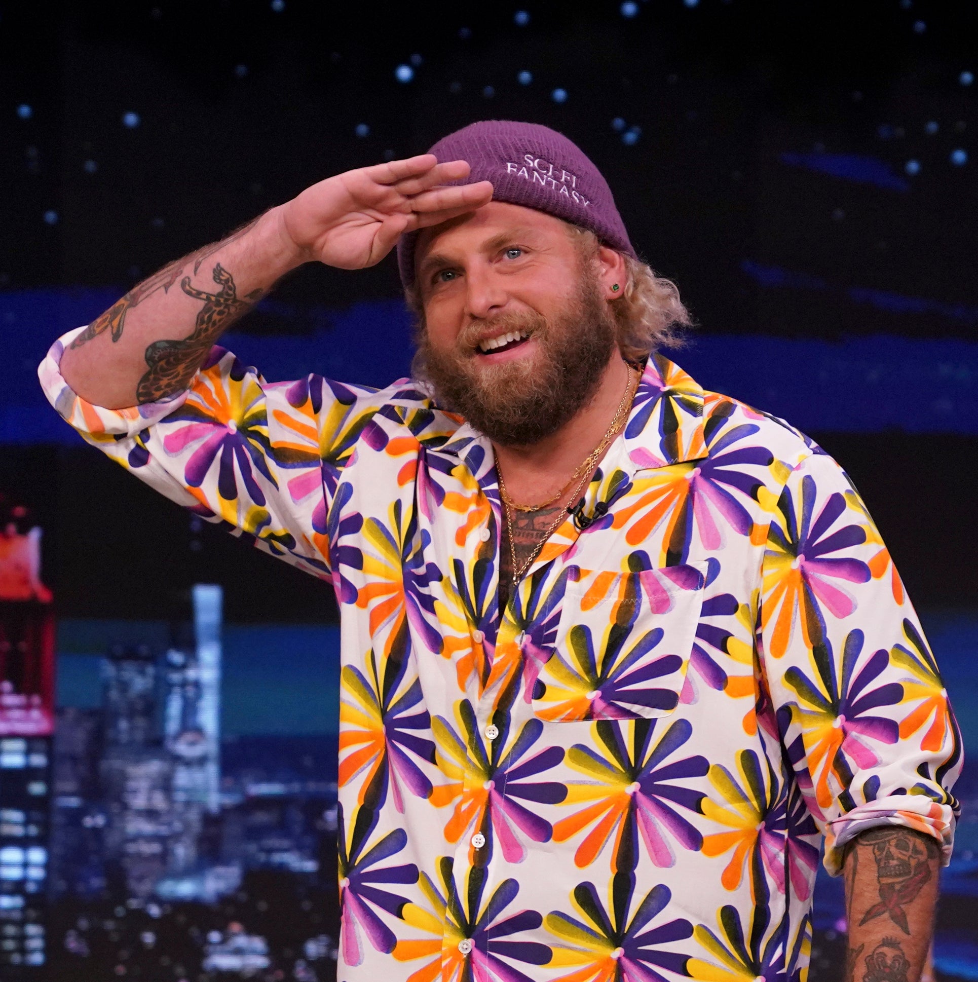 Close-up of Jonah in a bright print shirt and saluting on a talk show