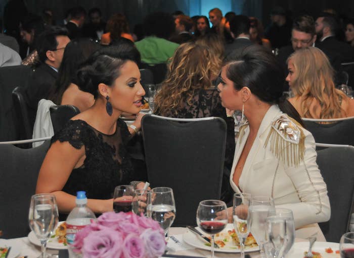 A closeup of Francia and Selena talking to each other as they sit at a table during an event