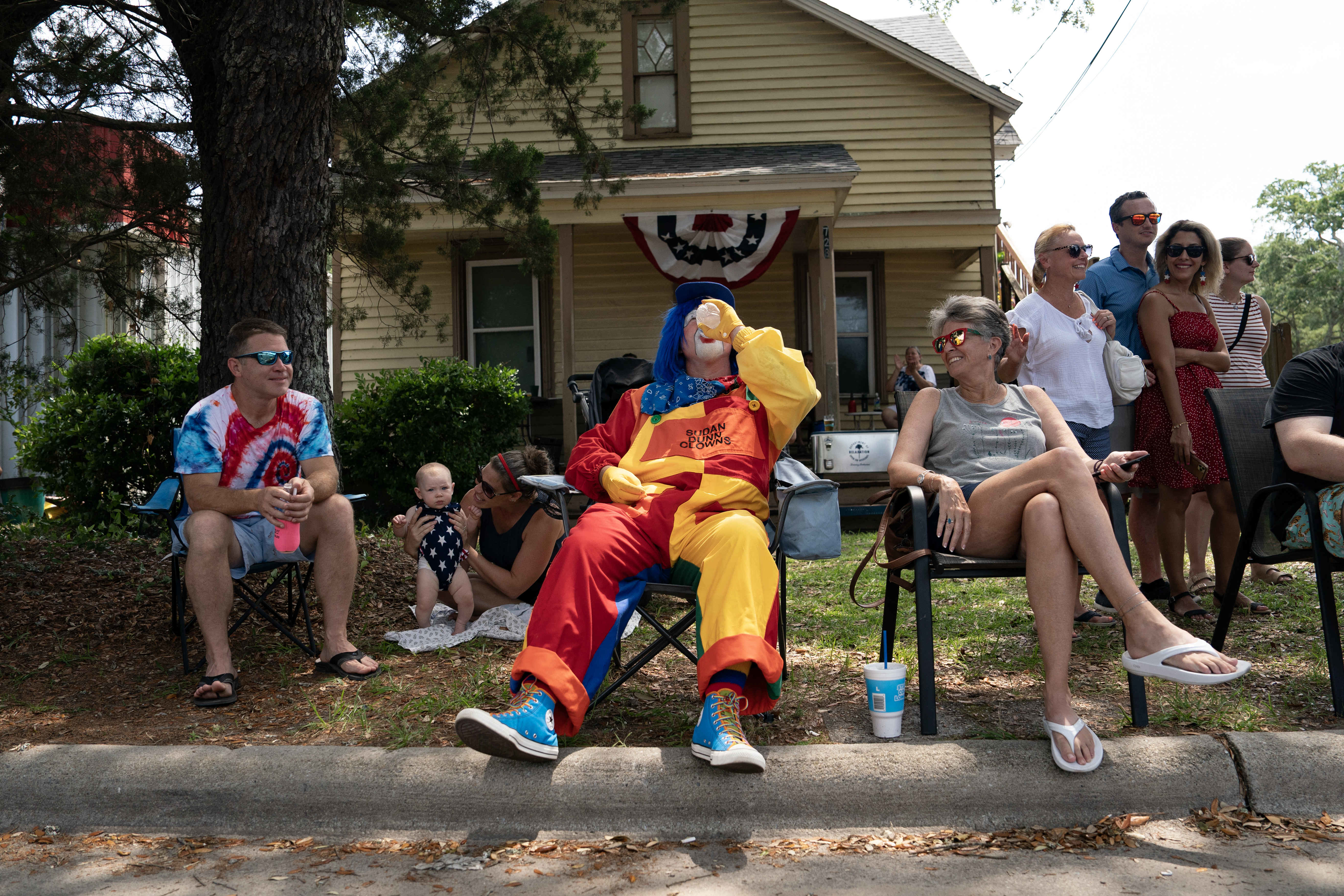 People, including someone in a clown costume, sitting outside of a house