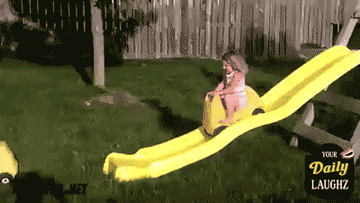 A child coming down a slide in a small toy truck and rolling over on the grass