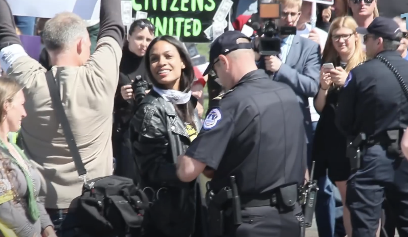 Closeup of Rosario Dawson smiling and being confronted by police
