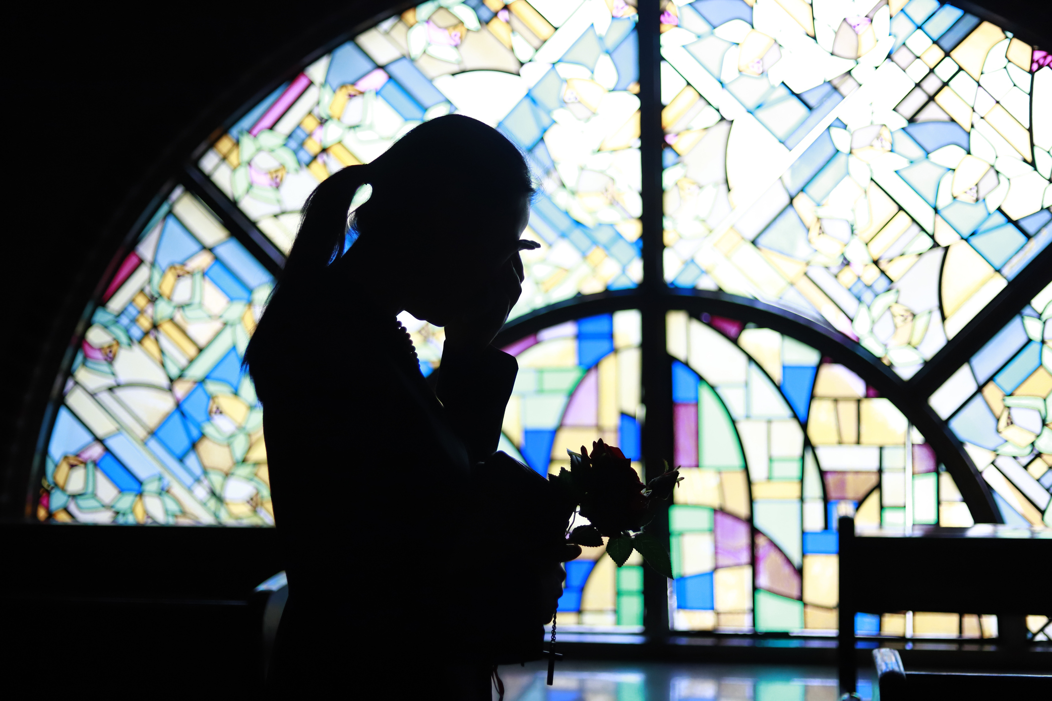 Silhuett av en person som holder blomster foran et stort, intrikate glassmalerier