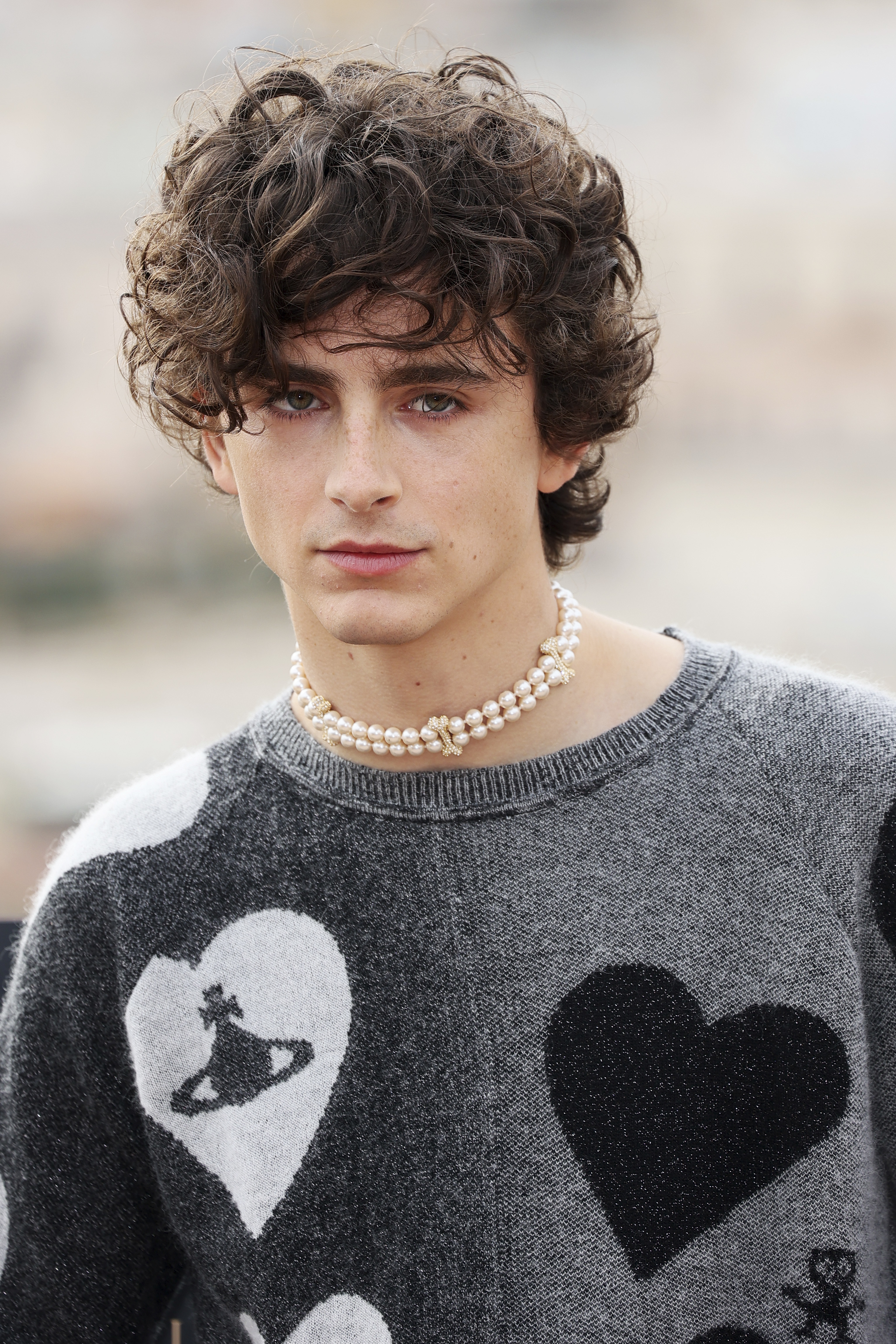 A close-up of Timothée in a heart-themed crewneck sweater and pearl choker