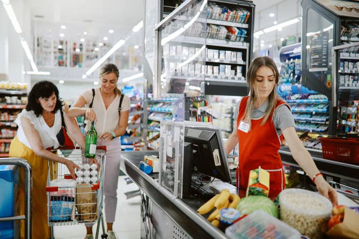 Senior woman with her daughter shopping in a large supermarket and handing groceries to the cashier