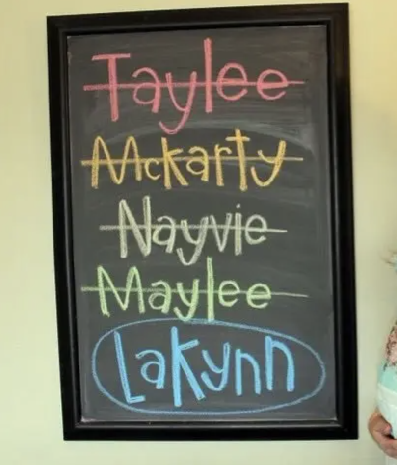 The names on the chalkboard are Taylee, McKarty, Nayvie, Maylee, and Lakynn. All of the names except Lakynn spelled L A K Y N N are crossed out
