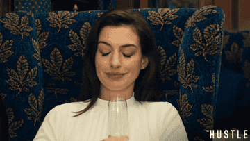 Anne Hathaway in &quot;The Hustle&quot; clinking her glass in the air