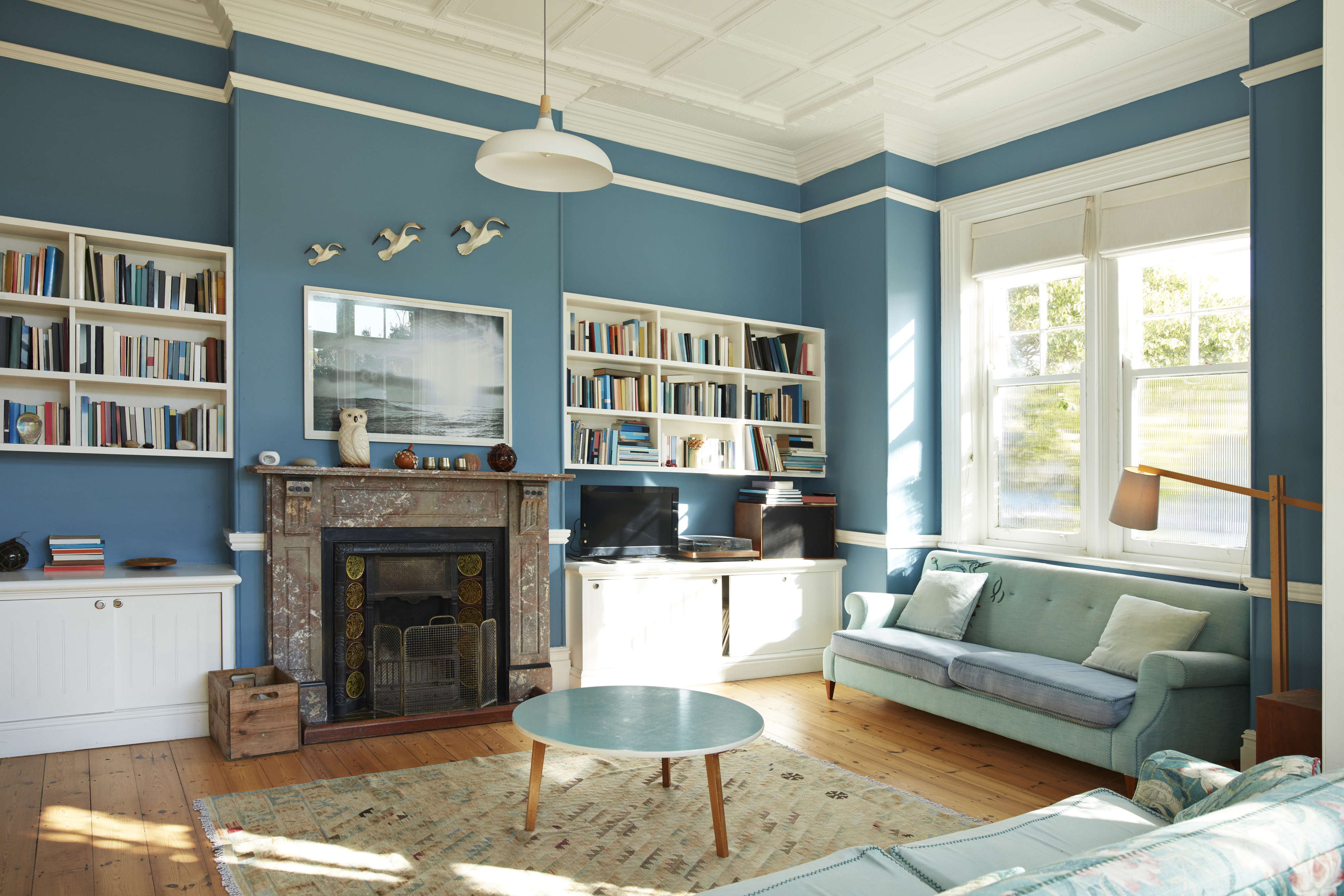 A living room with blue walls, matching furniture, a fireplace, and natural light