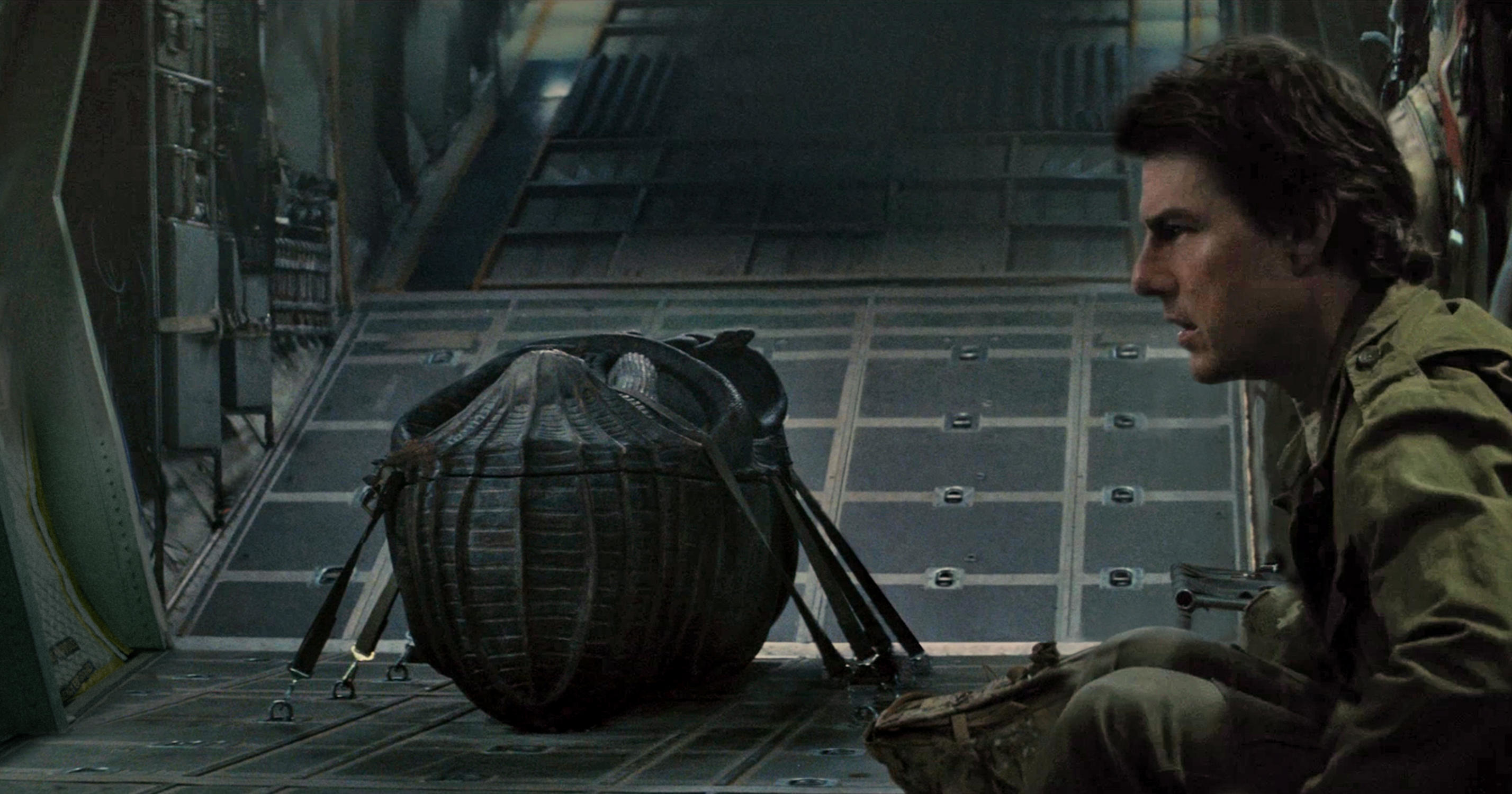 Tom Cruise sits on a military cargo plane near a large ornate coffin