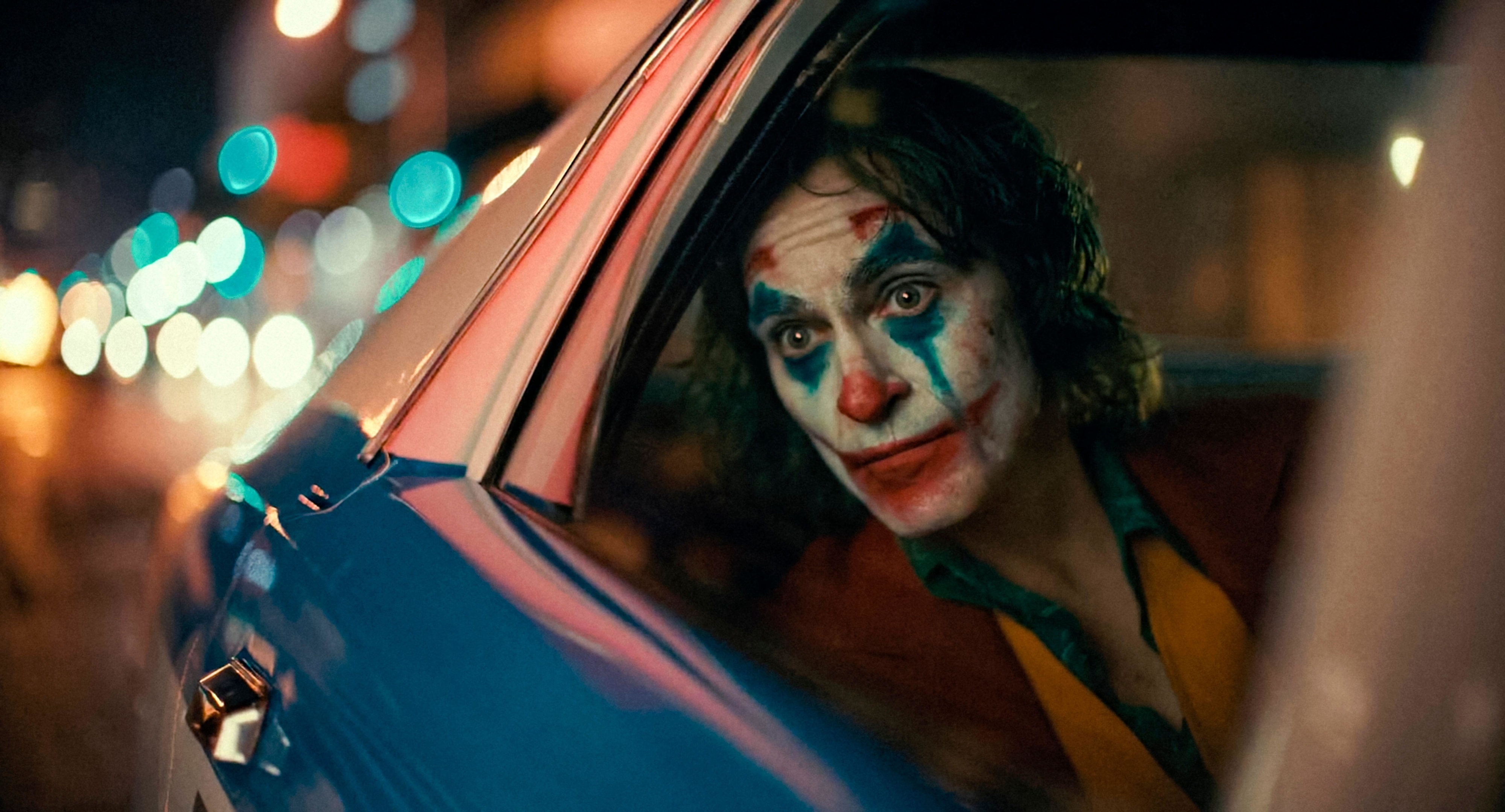 Joaquin Phoenix wears clown make-up while sitting in a cop car in &quot;Joker&quot;