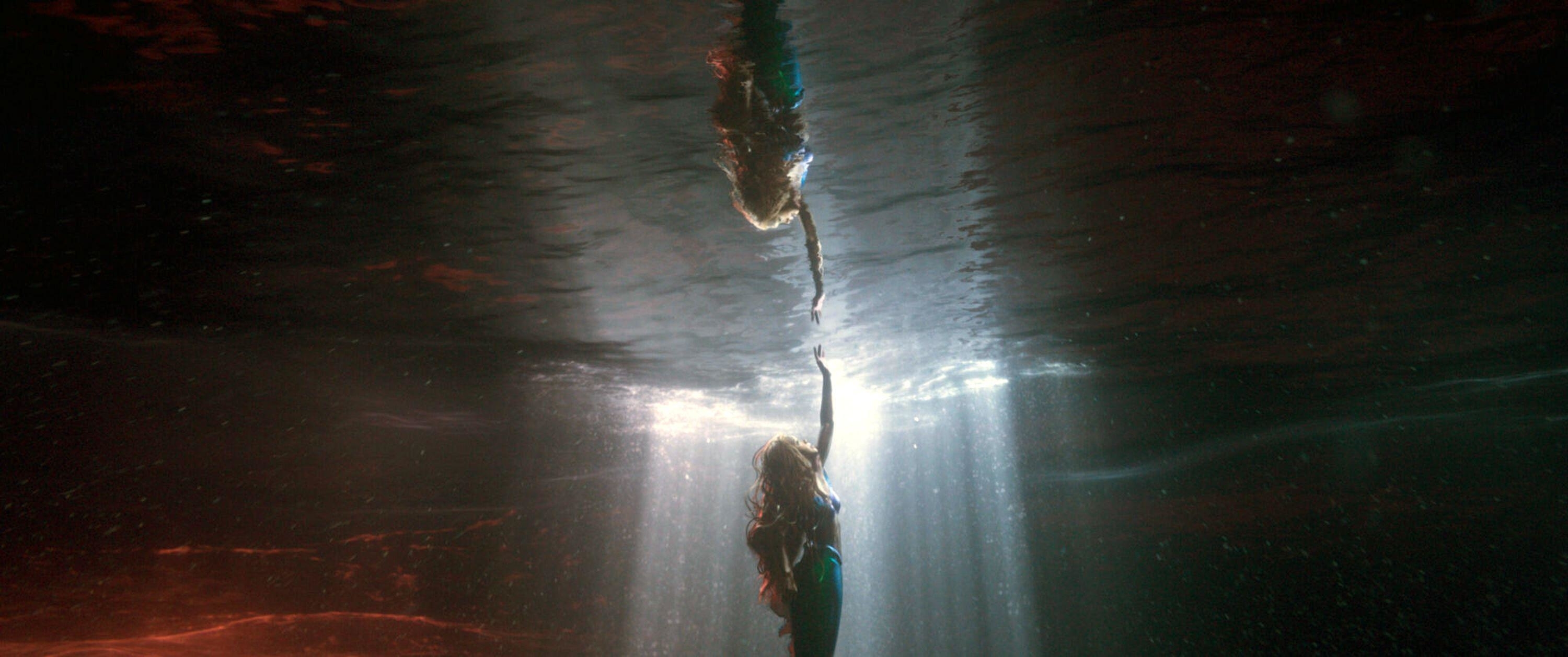 A mermaid reaches out to a spot of light peaking through the ocean surface