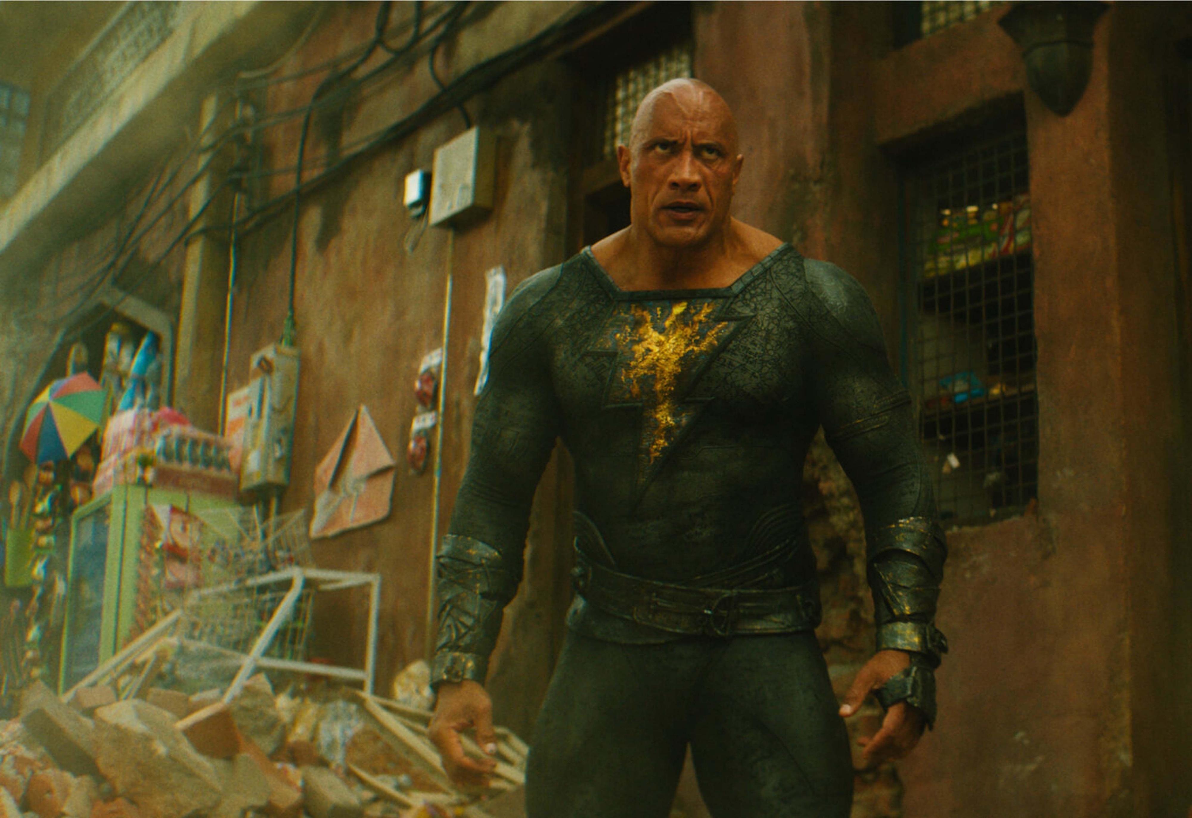 Dwayne Johnson stands in the street of a desert city wearing a blackened Shazam costume
