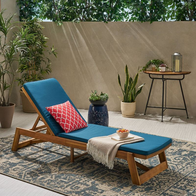the chaise in teak/blue with an accent pillow on it