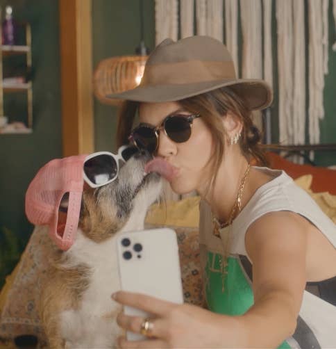 A dog and owner kiss wearing hat and sunglasses