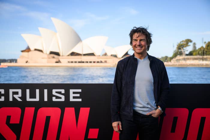 Close-up of Tom smiling with Mission: Impossible poster behind him and the Sydney Opera House in the background