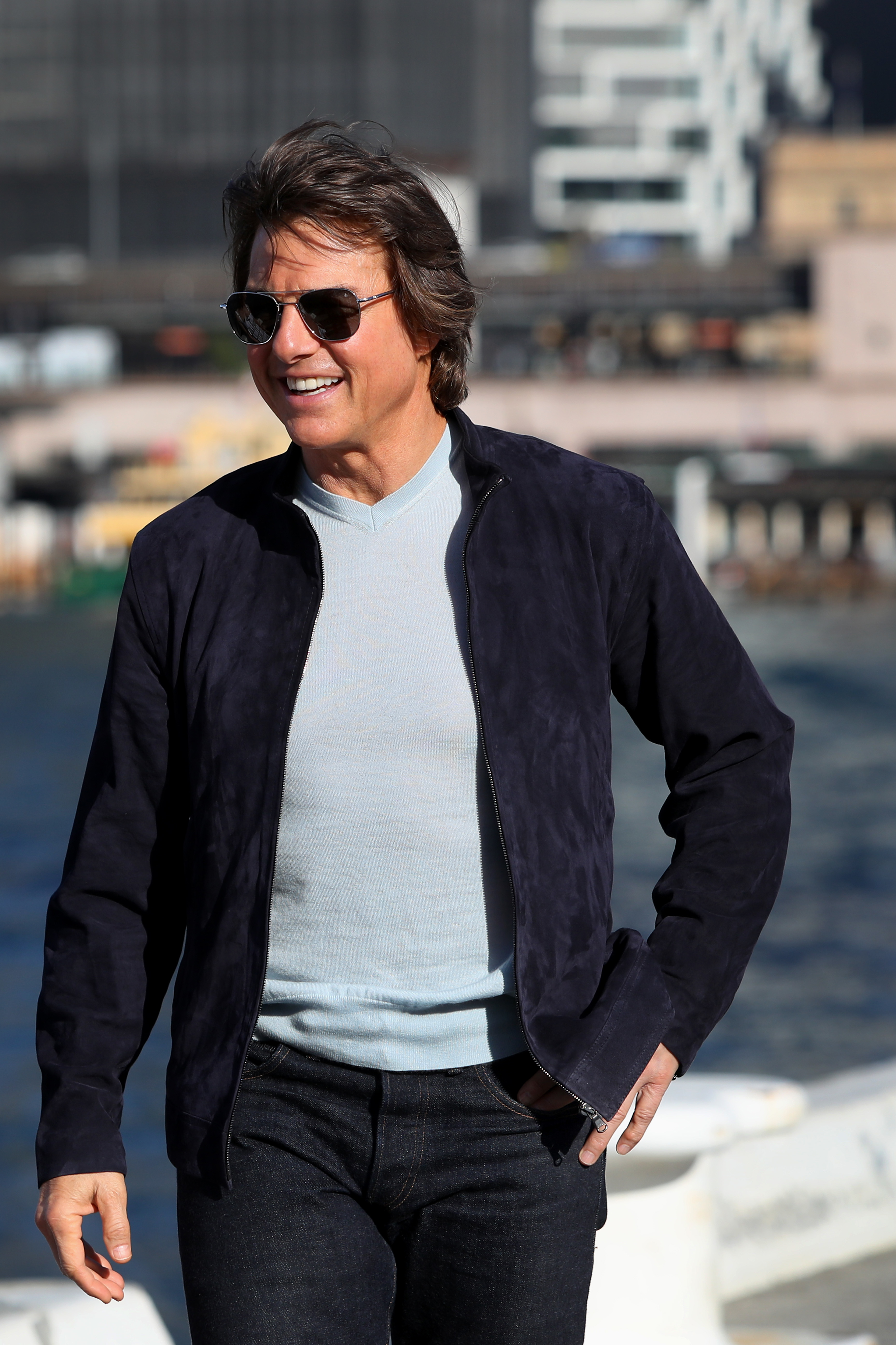 Close-up of Tom smiling and wearing sunglasses, a jacket, a T-shirt, and jeans