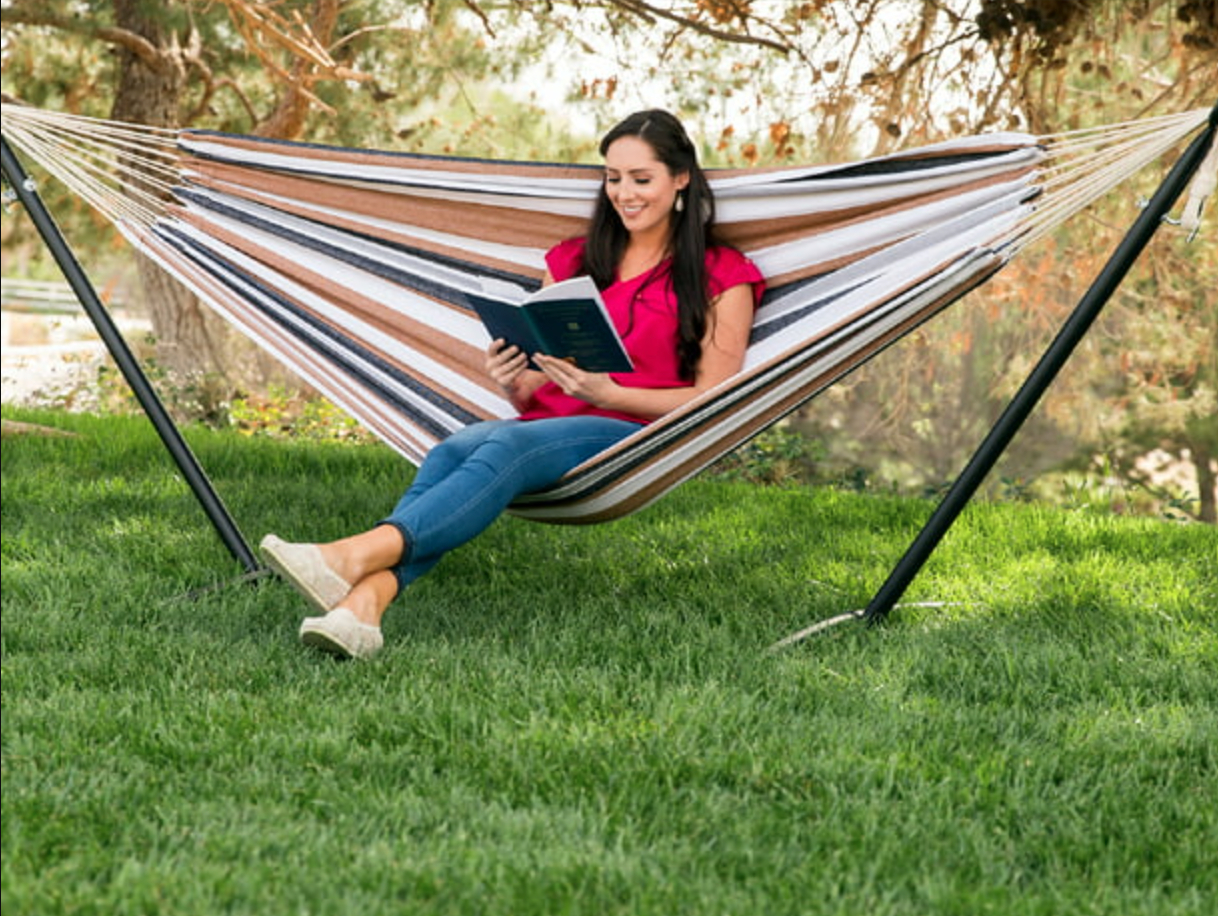 a model reading a book in the striped hammock in a backyard