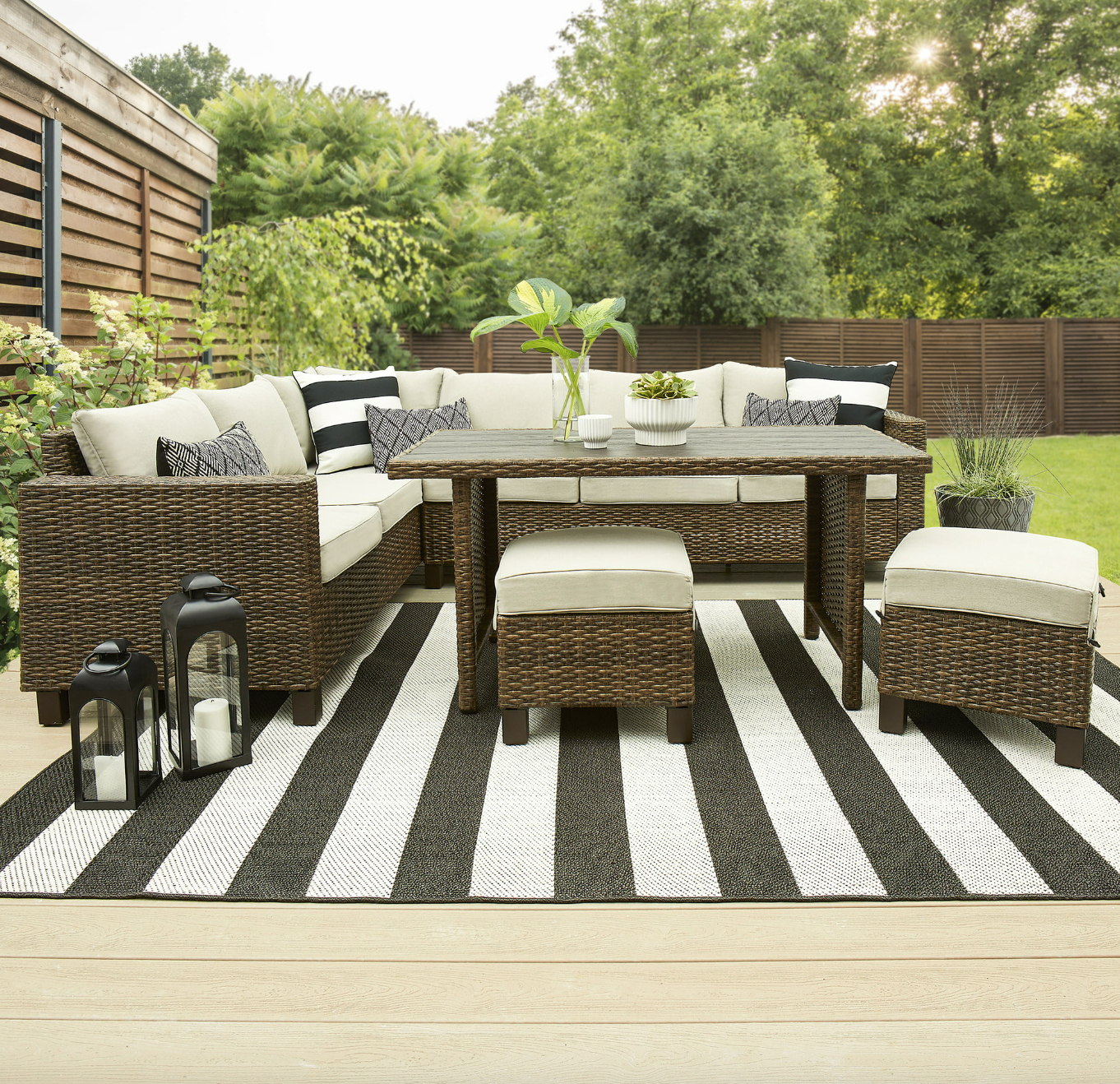 the dark wicker sectional, dining table and ottomans with tan cushions in a decorated patio space