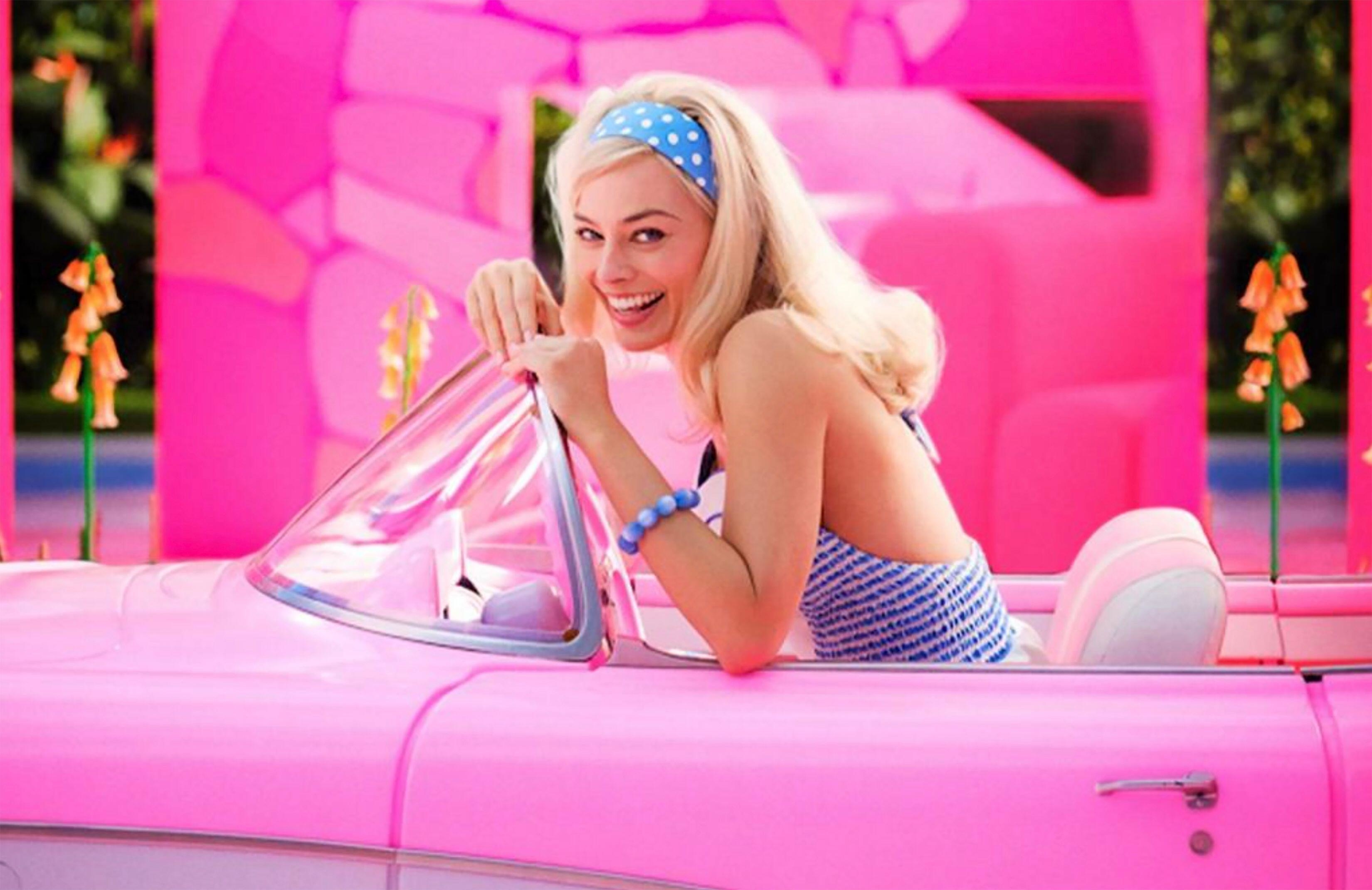 Margot Robbie as Barbie in a pink convertible car in the movie
