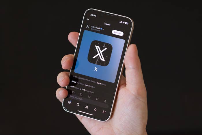 A hand holding a smartphone with the X app