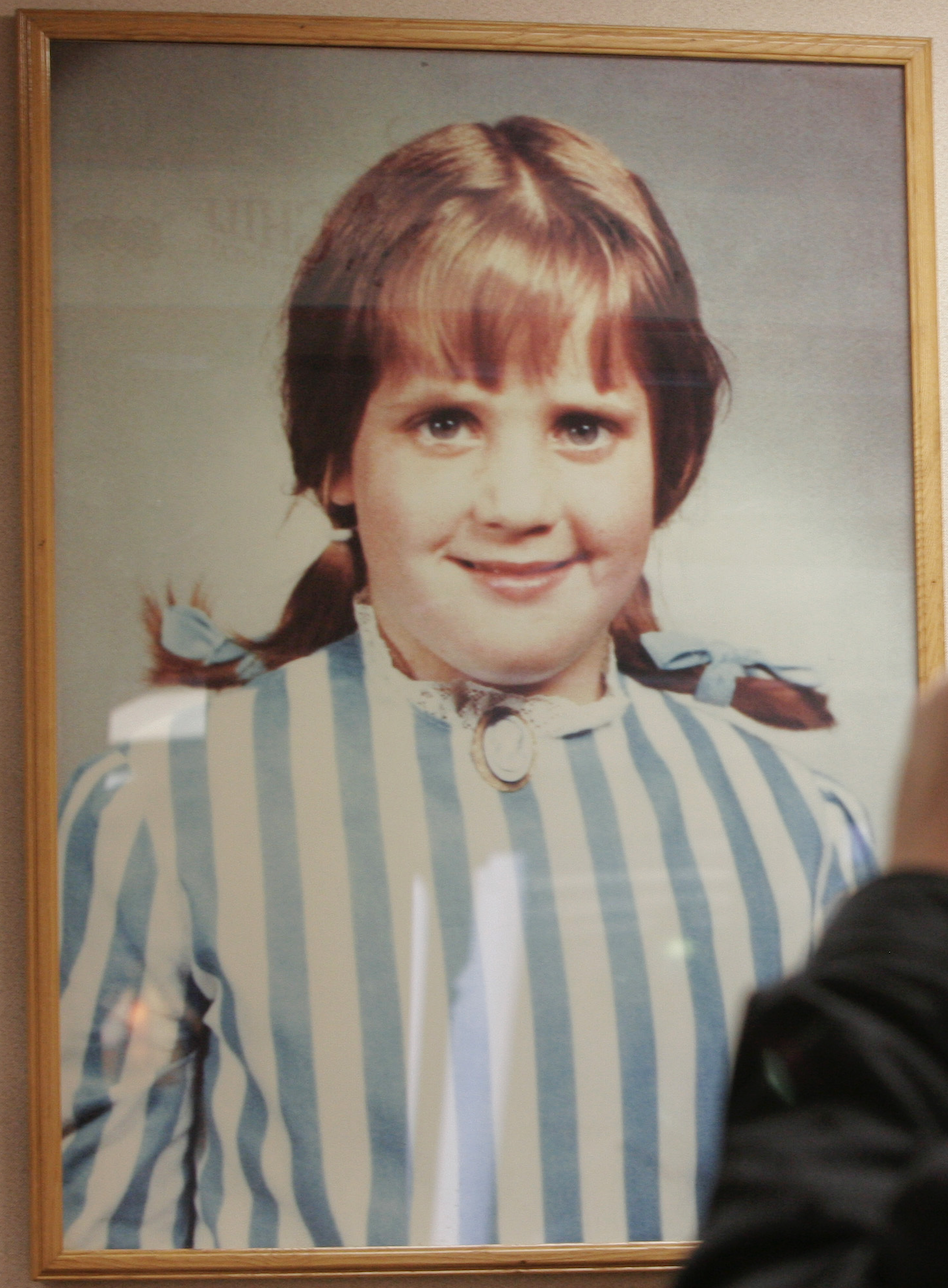 A smiling young girl in pigtails, bangs, and a striped blouse