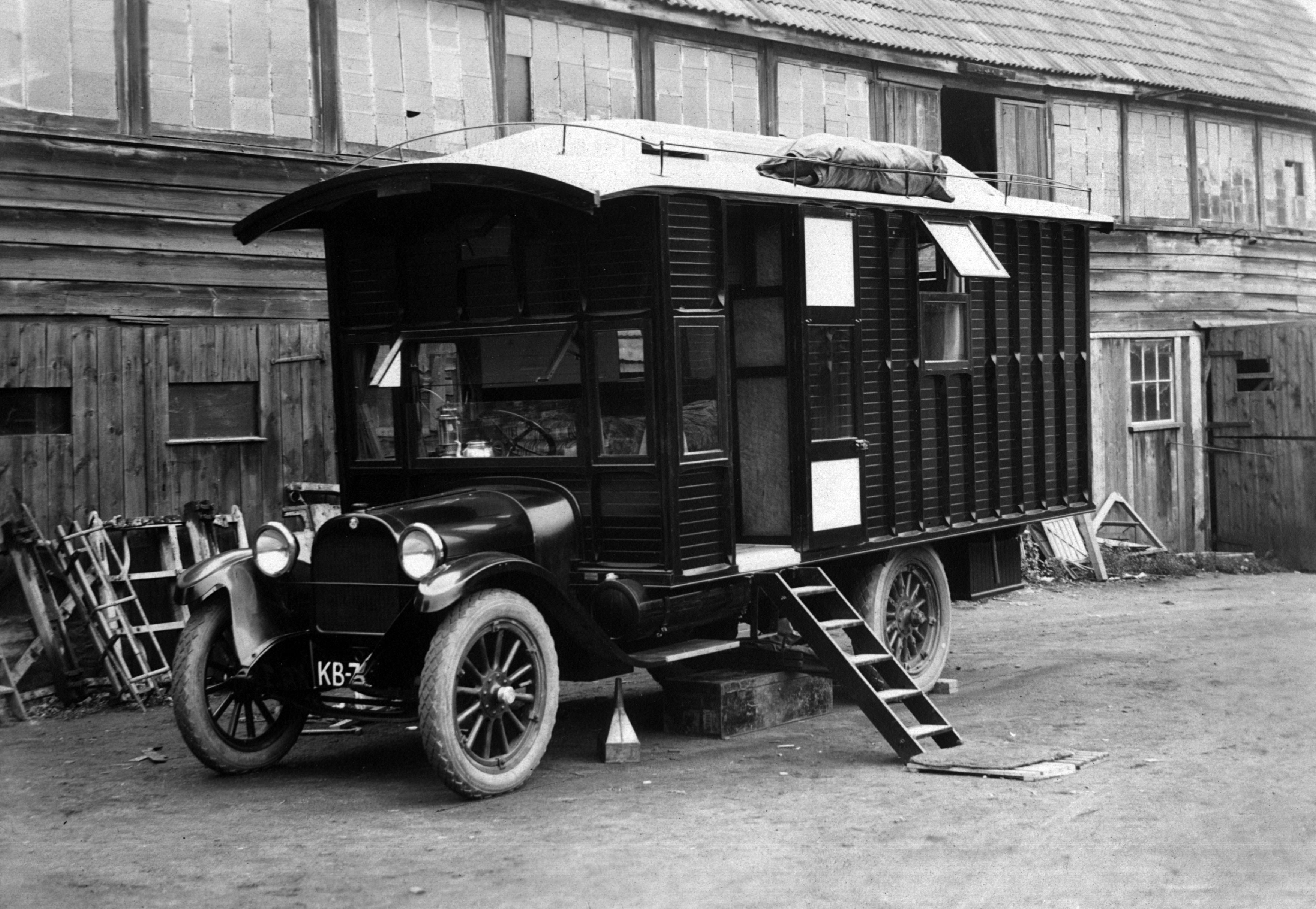 A covered wagon–type trailer car with a small ladder on the side