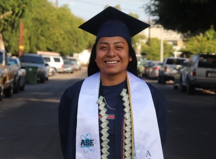 A recent, smiling high school graduate posing for a picture