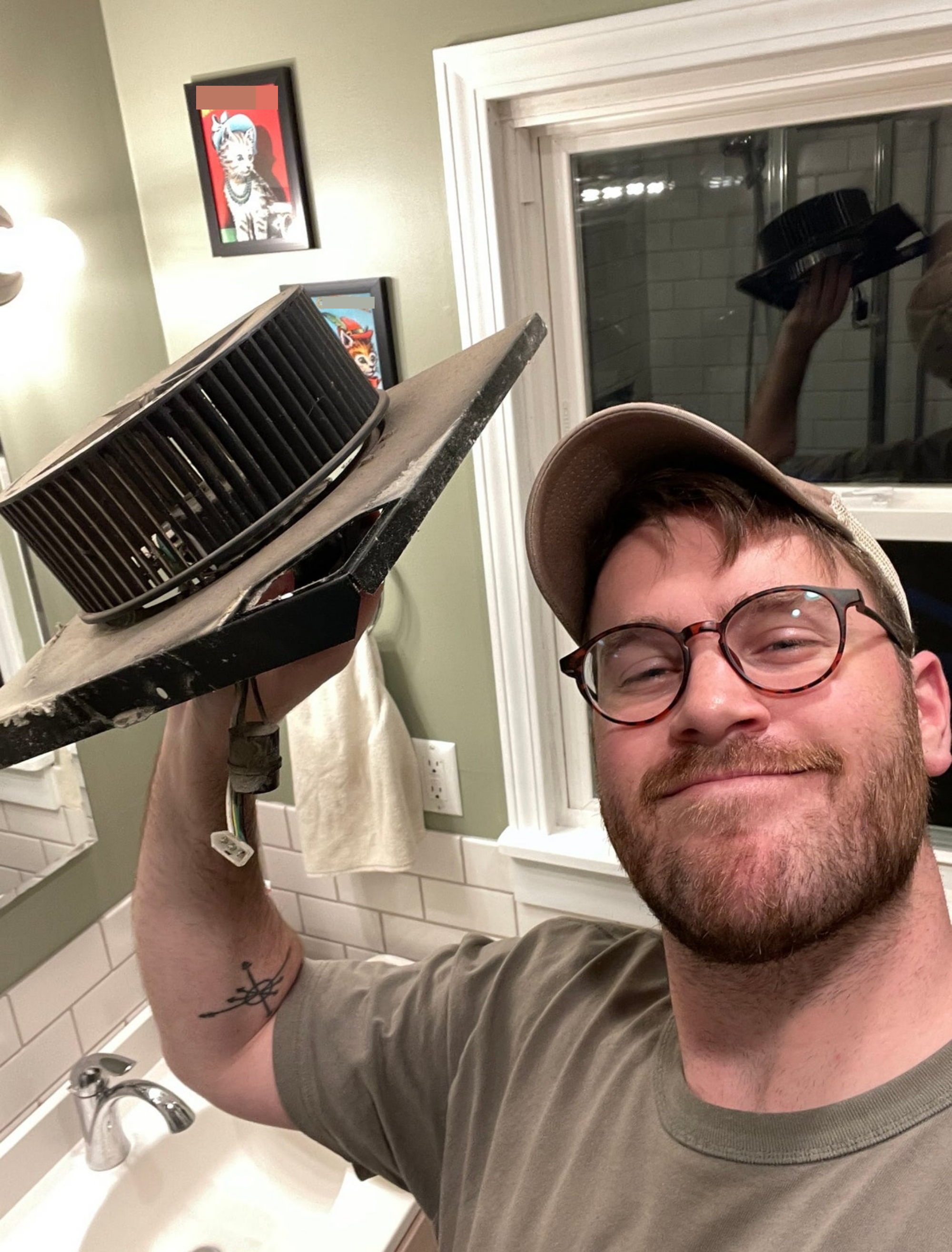 author holding up fan assembly in bathroom while replacing it