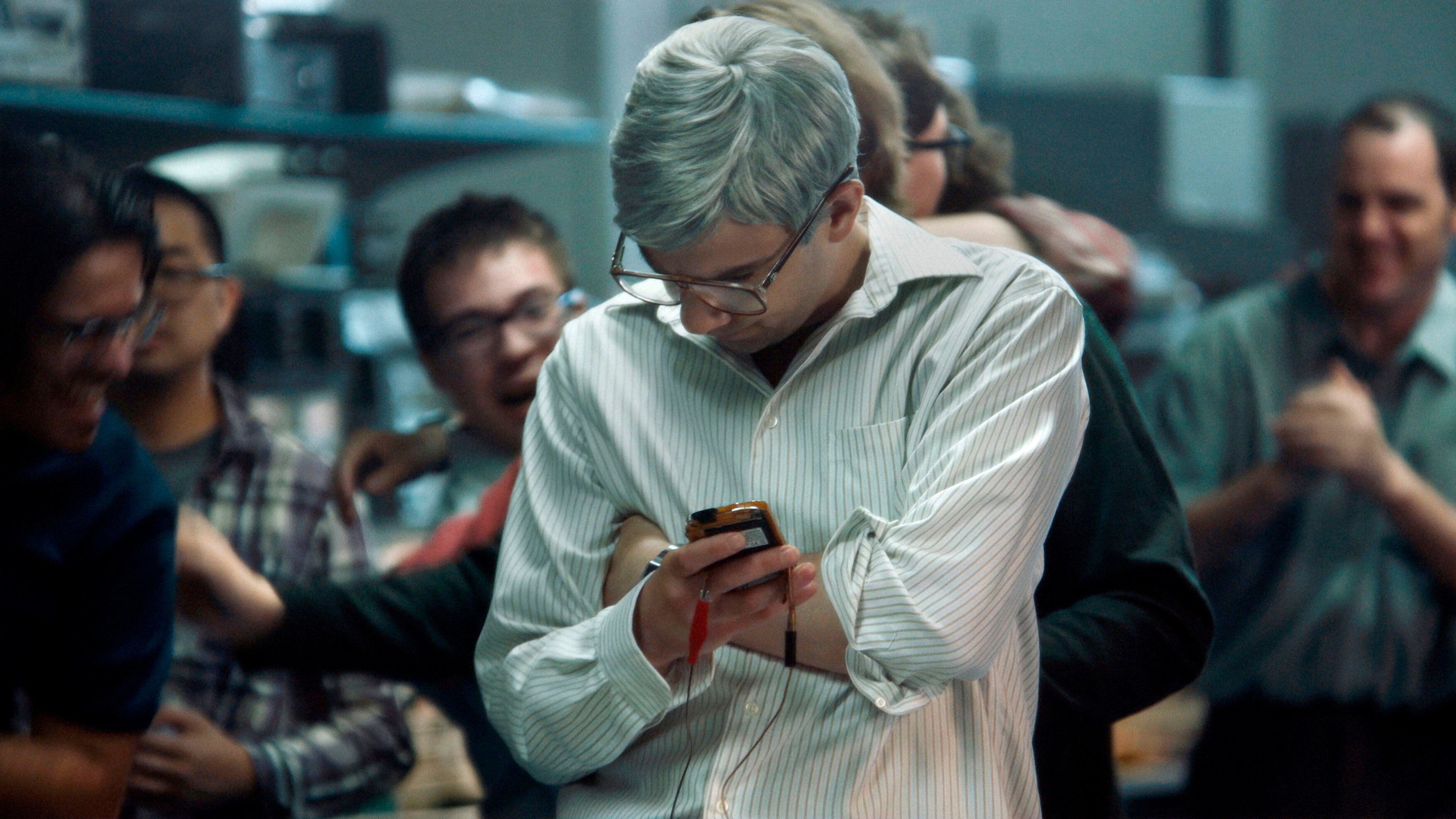 A grey-haired man with glasses closely examines a prototype cell phone
