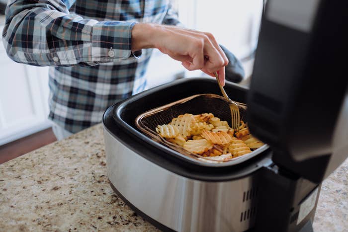 person cooking waffle fries in an air fryer
