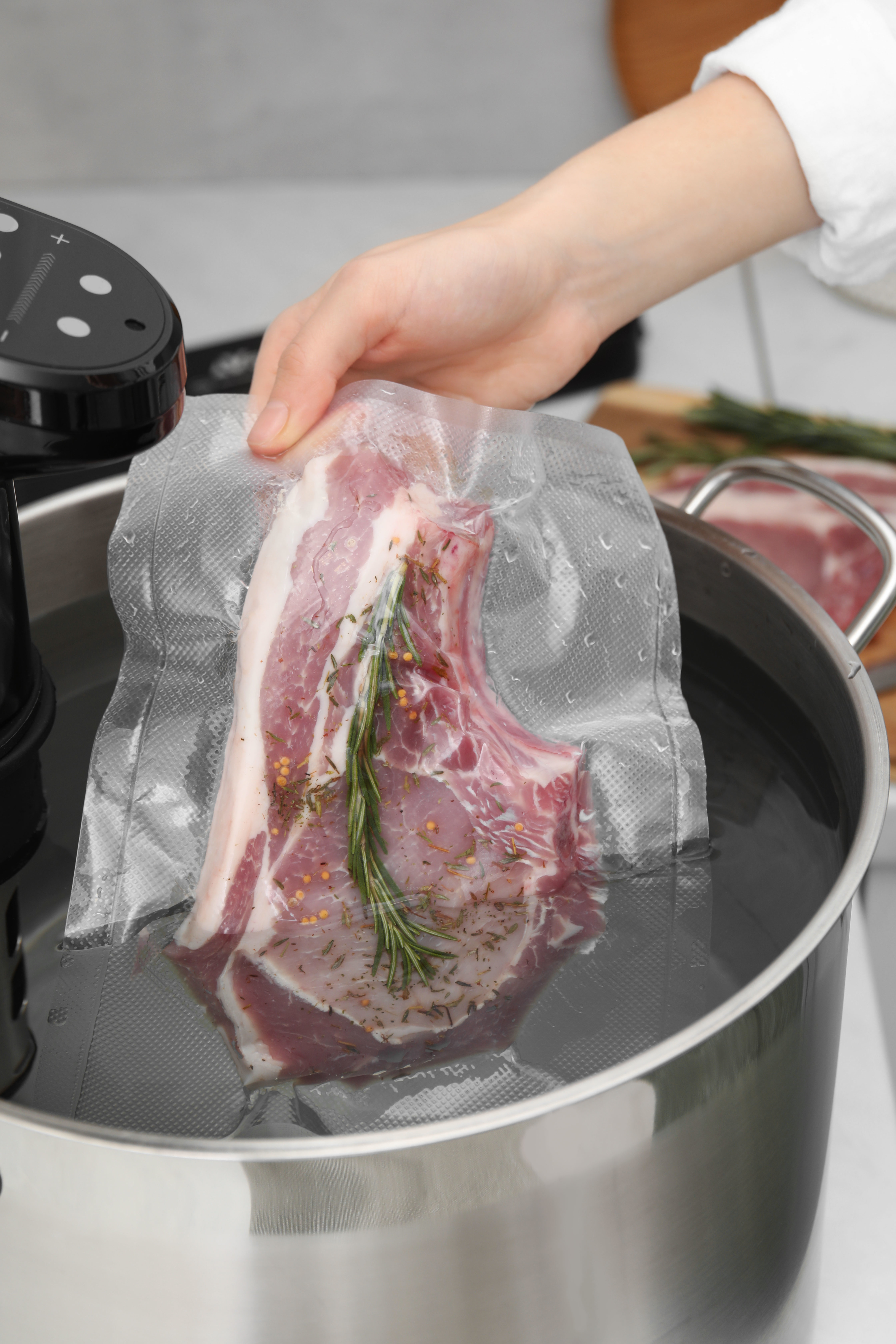 woman putting vacuum sealed meat into a sous vide cooker