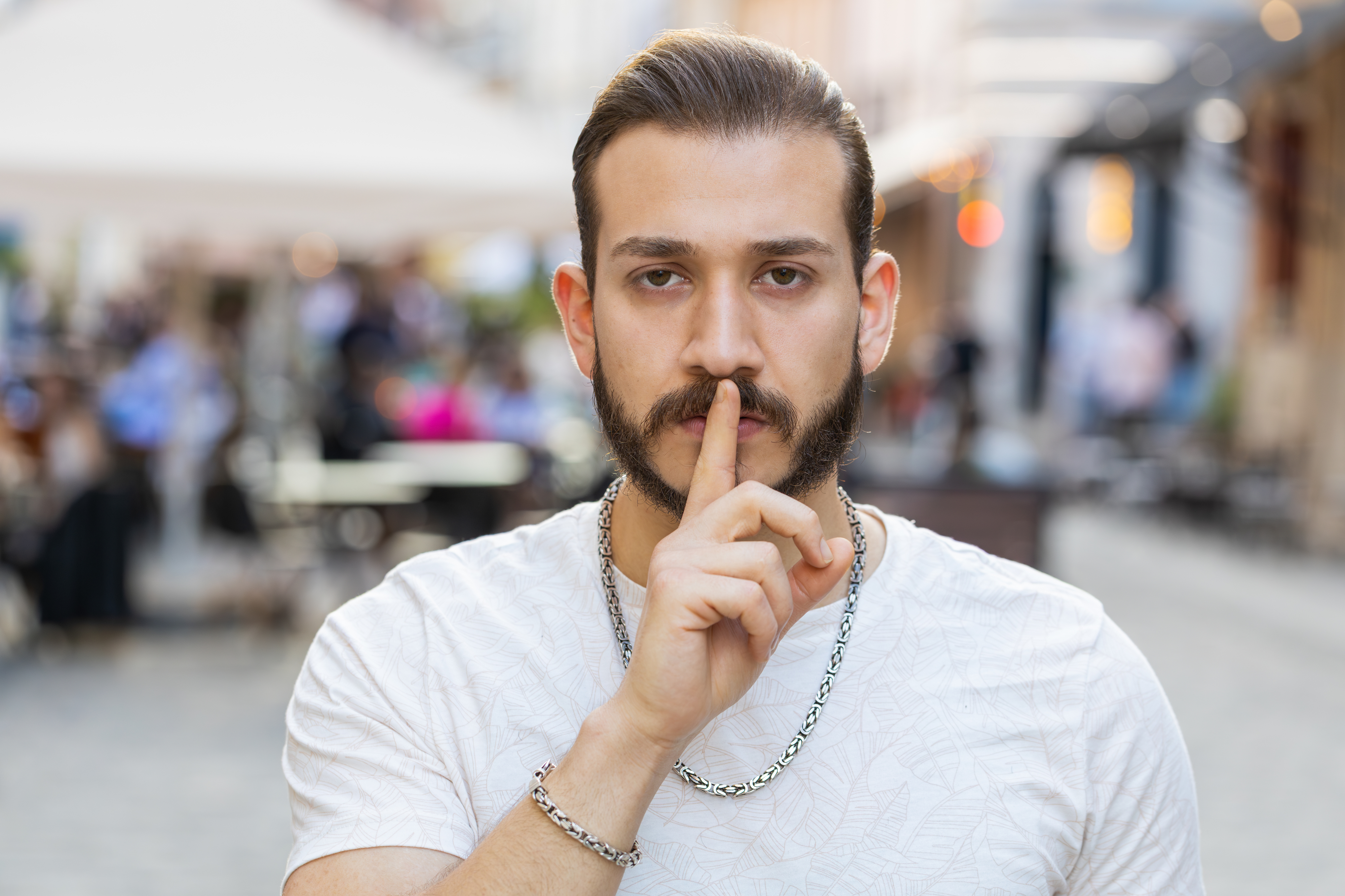 Shh be quiet please. Bearded young adult man presses index finger to lips makes silence hush gesture sign do not tells gossip. Guy walking in urban city sunshine street. Town lifestyles