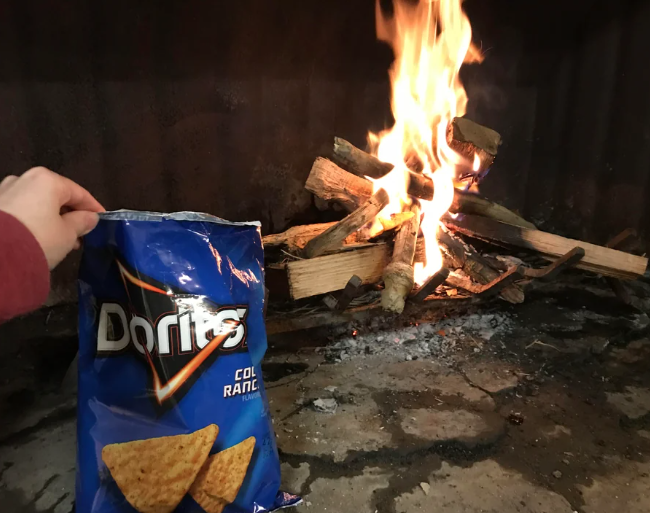 Someone holding a bag of Doritos in front of a campfire