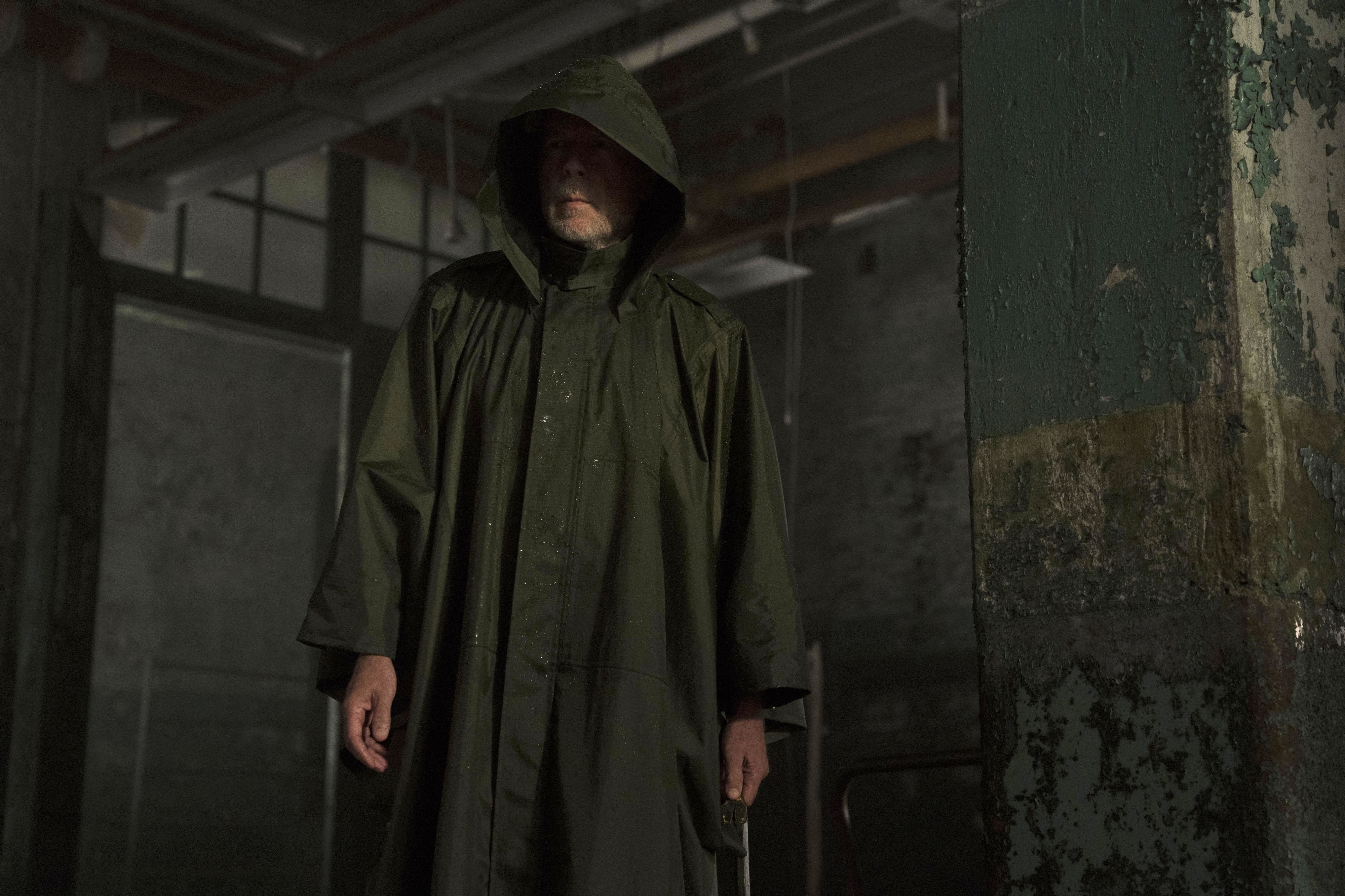 Bruce Willis wears a grey raincoat in a decrepit factory