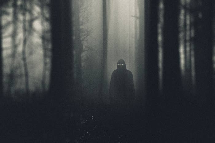 A dark hooded figure with glowing eyes standing in a forest