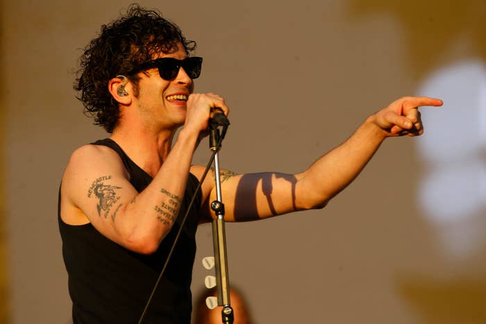 Matty Healy performing onstage in a tank top and sunglasses