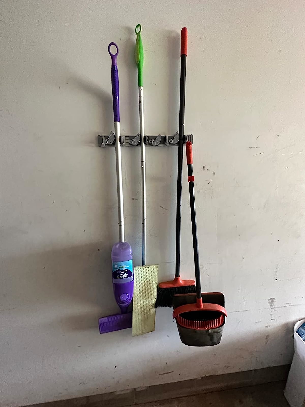 Reviewer's swiffer, brooms, and mop hanging in holder on wall