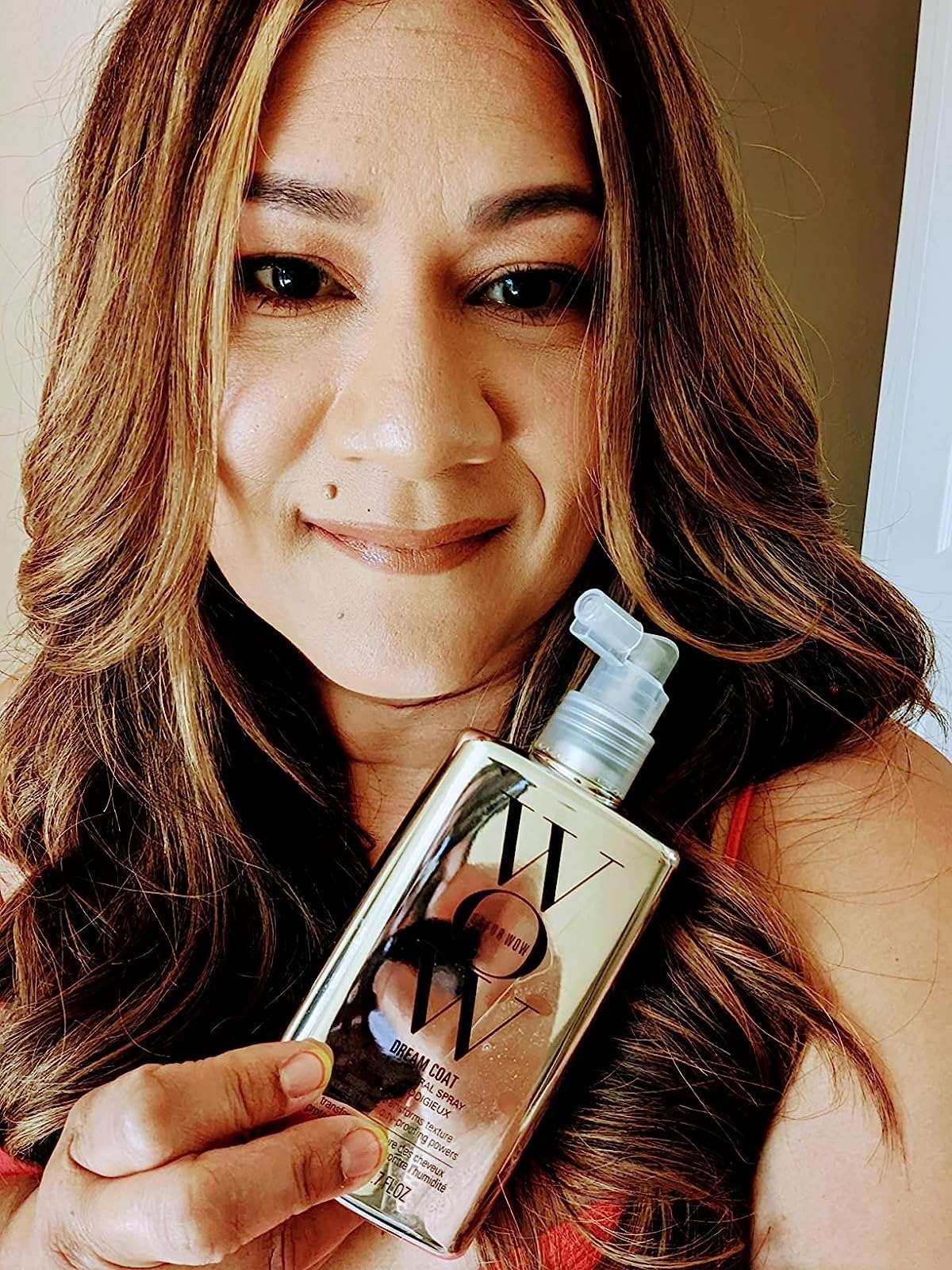 reviewer with shiny brown highlighted hair holding a bottle of the hair treatment