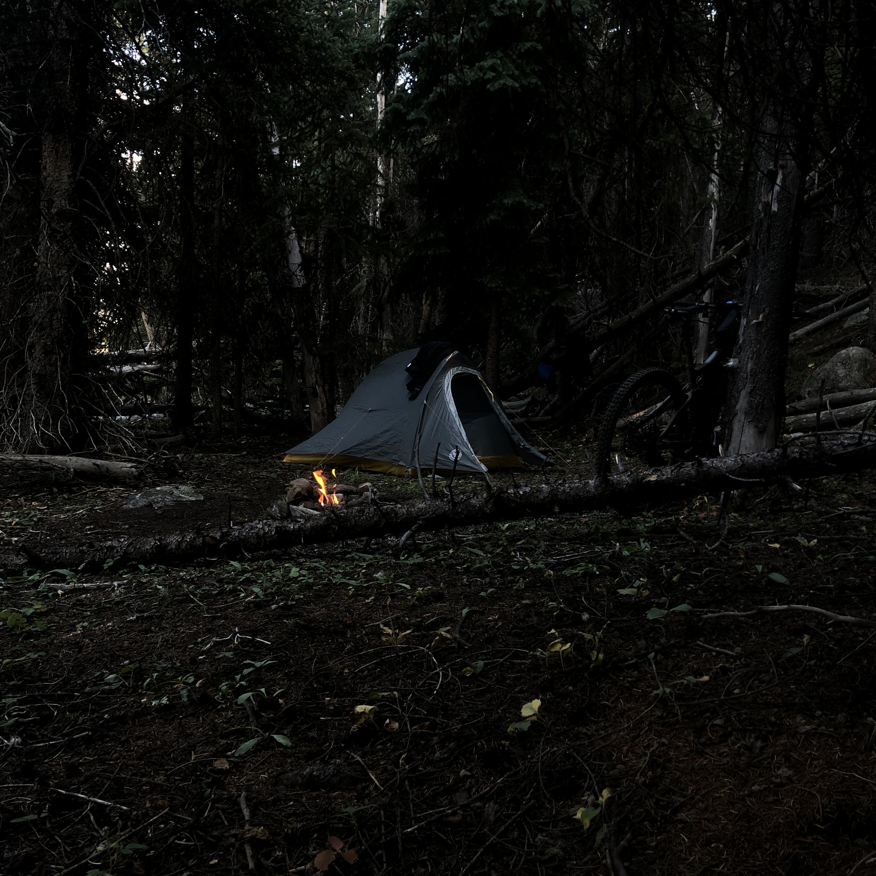 Tent in the woods with a fire next to it