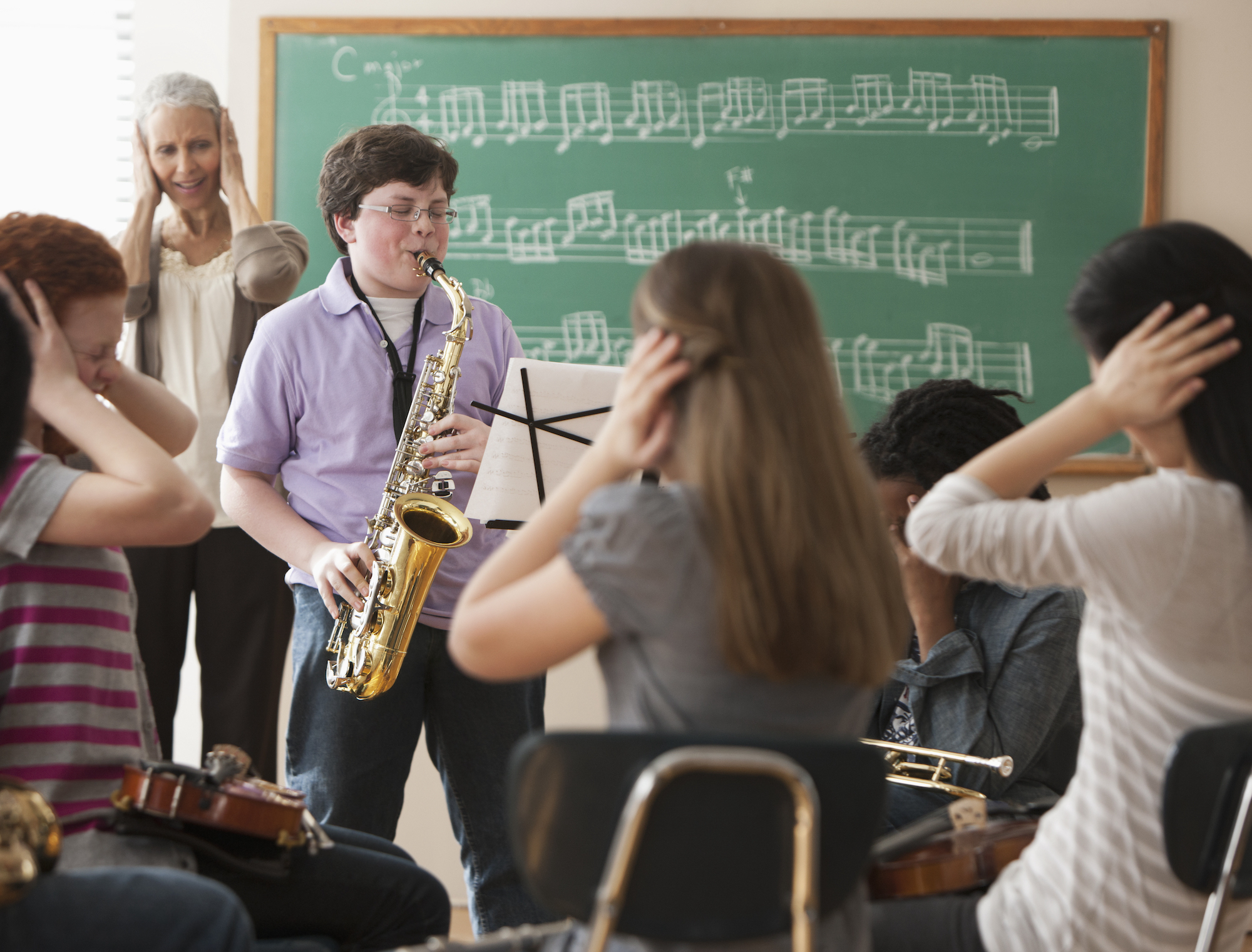 A young boy playing the saxophone as his class covers their ears