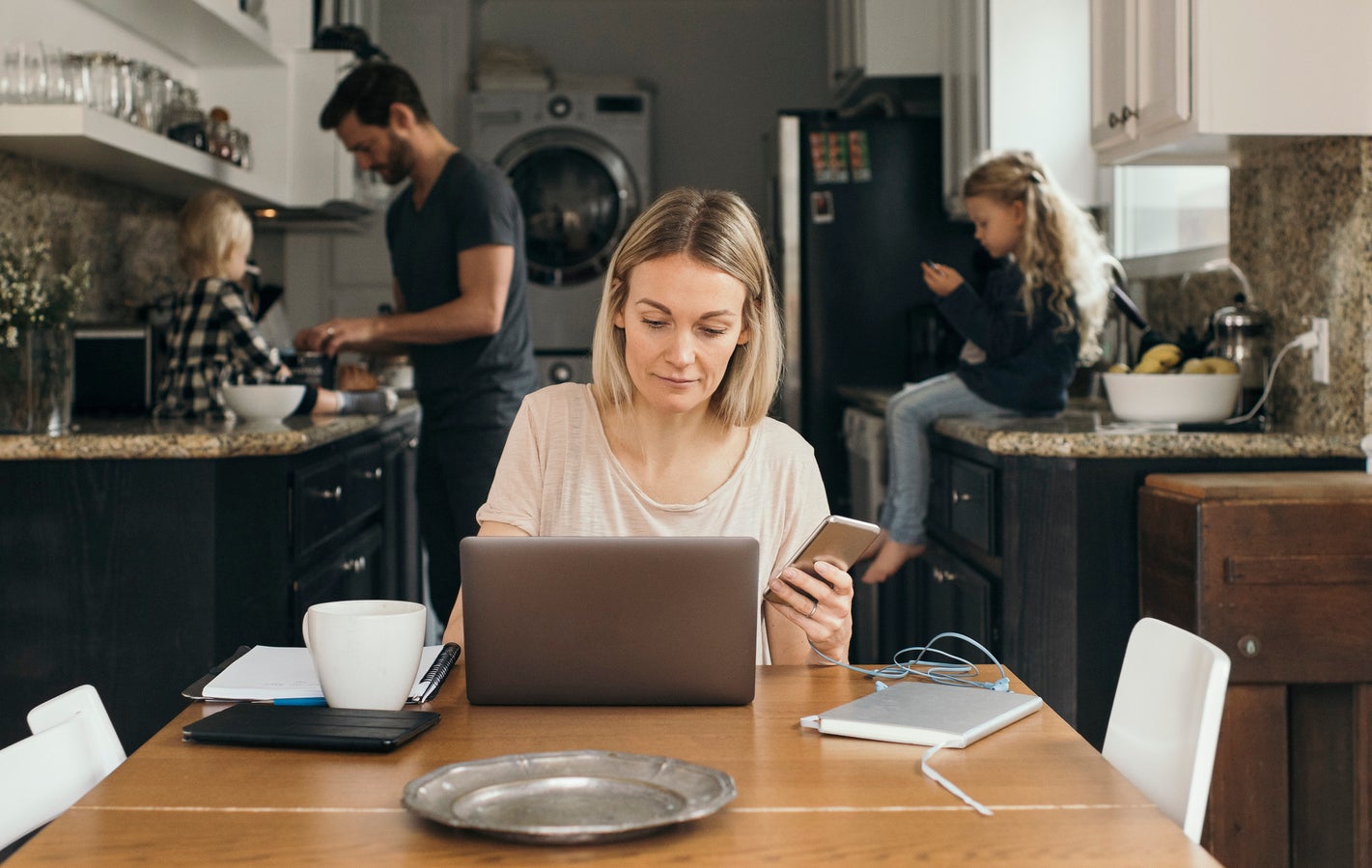 Woman researches on computer while dad cares for kids behind her